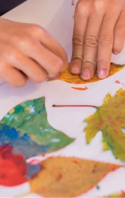 Fundación Planeta Tierra – Educación, Bienestar y Primera Infancia #de0a7 15 Manos de un niño realizando una actividad artística con hojas pintadas sobre papel, integrando naturaleza y creatividad.