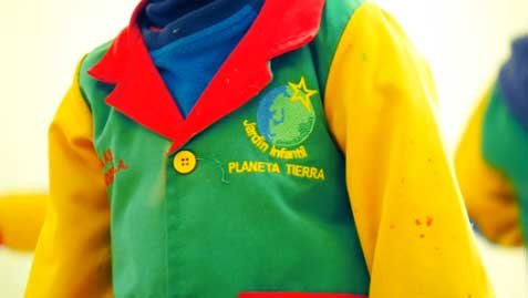 Nuestro Propósito | Fundación Planeta Tierra – Bienestar desde la infancia 5 Delantal verde, amarillo y rojo con insignia de Jardín Infantil Planeta Tierra, símbolo de identidad y pertenencia.